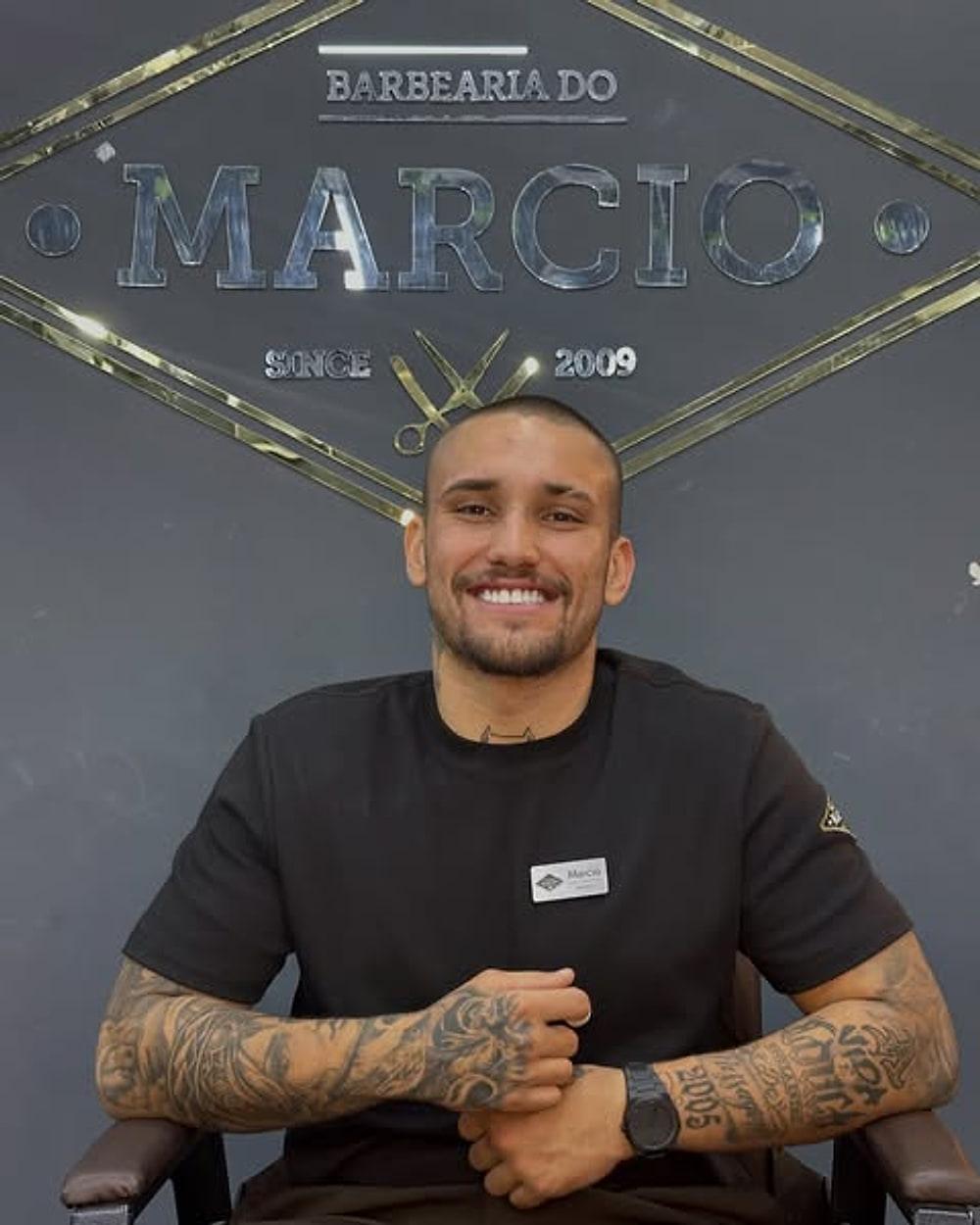 Cauan sentado na cadeira, sob o letreiro da barbearia