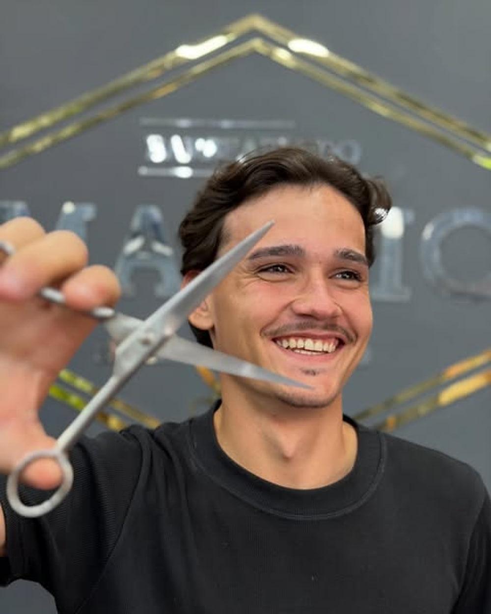 Matheus Lucena com a tesoura na mão, em frente ao letreiro da barbearia